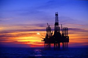 Silhouette of oil platform in sea against moody sky at sunset